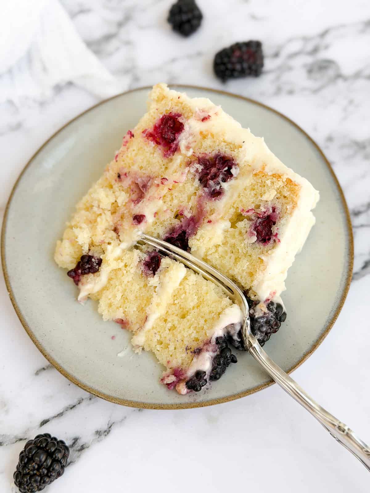 a slice of the lemon blackberry layer cake on a plate with a fork in it.