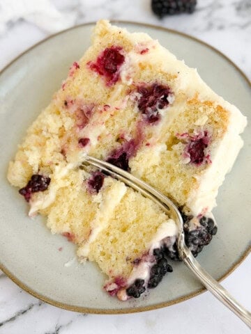 a slice of the lemon blackberry layer cake on a plate with a fork in it.