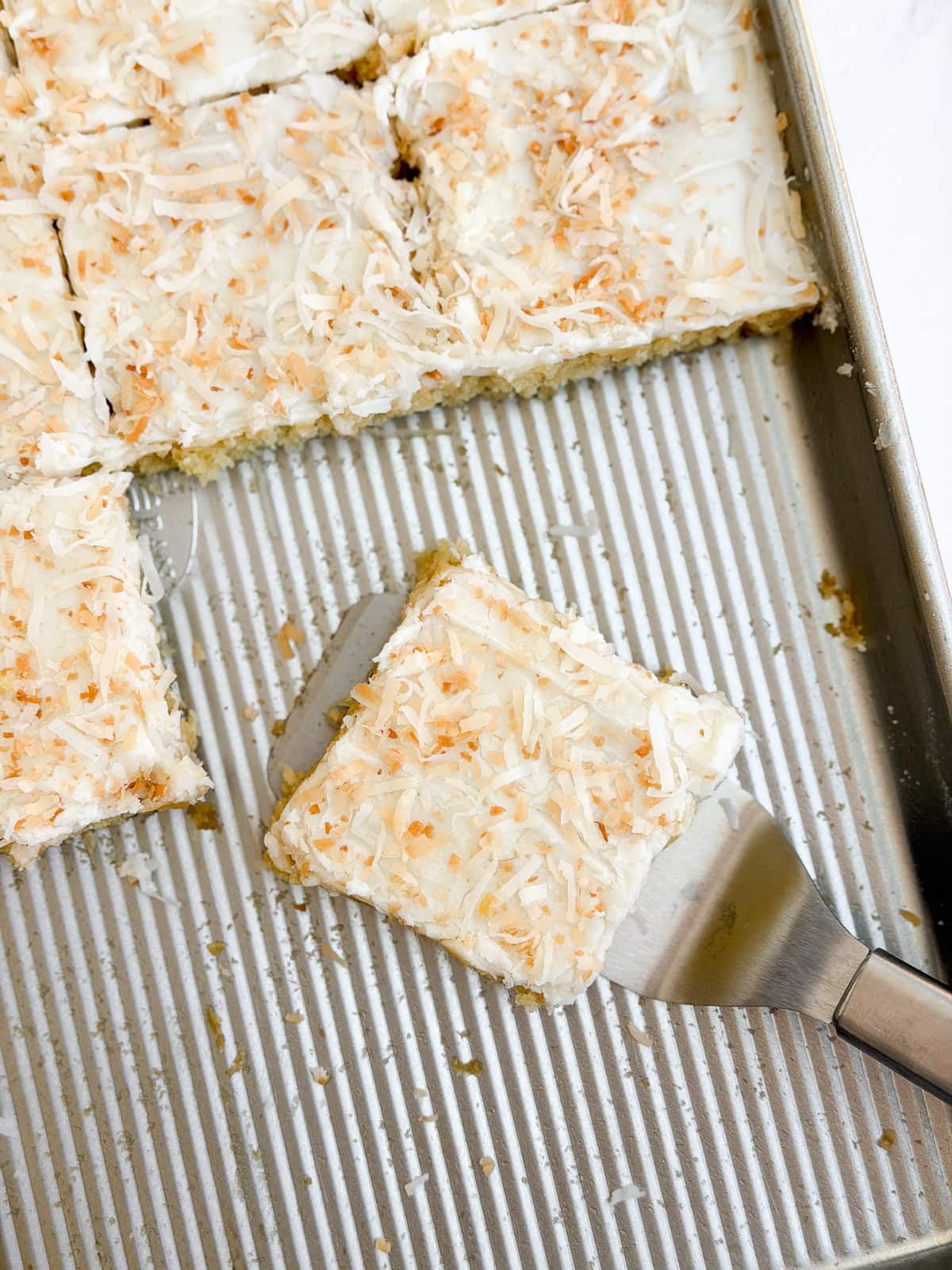 a few slices of coconut texas sheet cake on a cookie sheet after cutting.