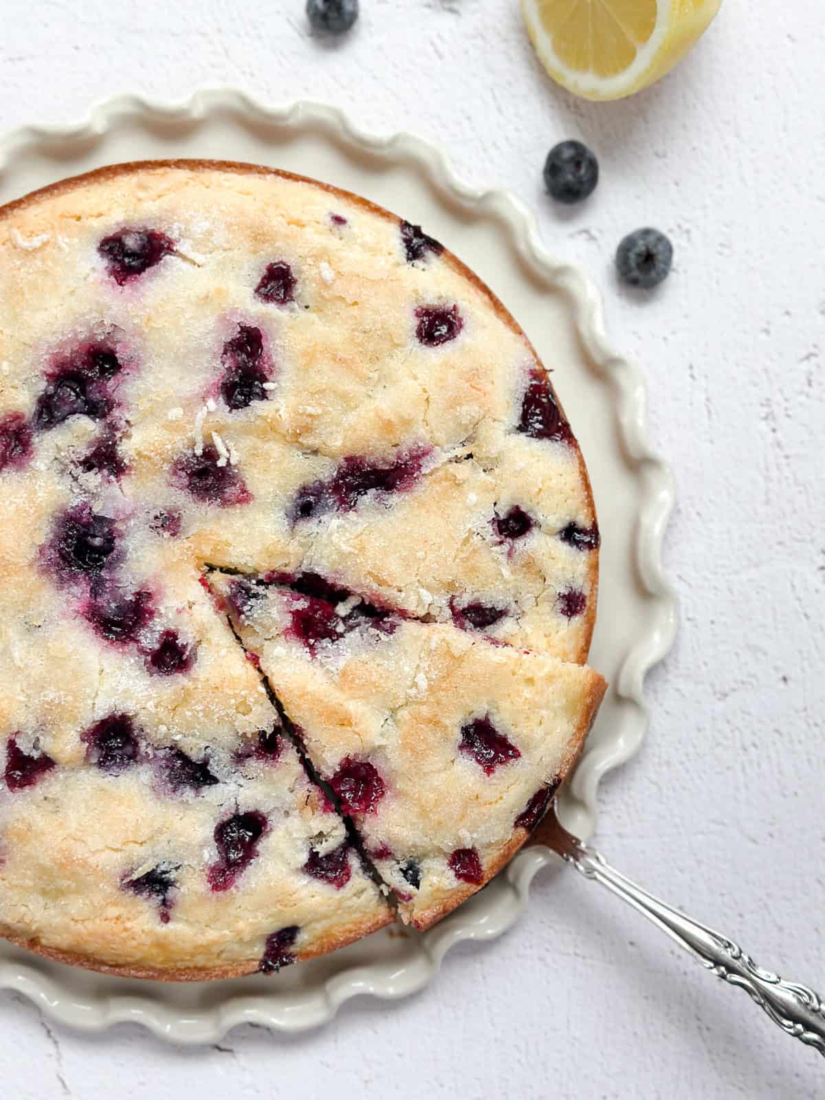 lemon blueberry sour cream cake on a cake plate with a spatula taking a piece.