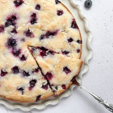 lemon blueberry sour cream cake on a cake plate with a spatula taking a piece.