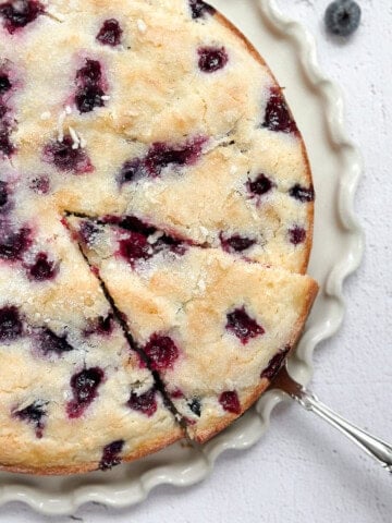 lemon blueberry sour cream cake on a cake plate with a spatula taking a piece.