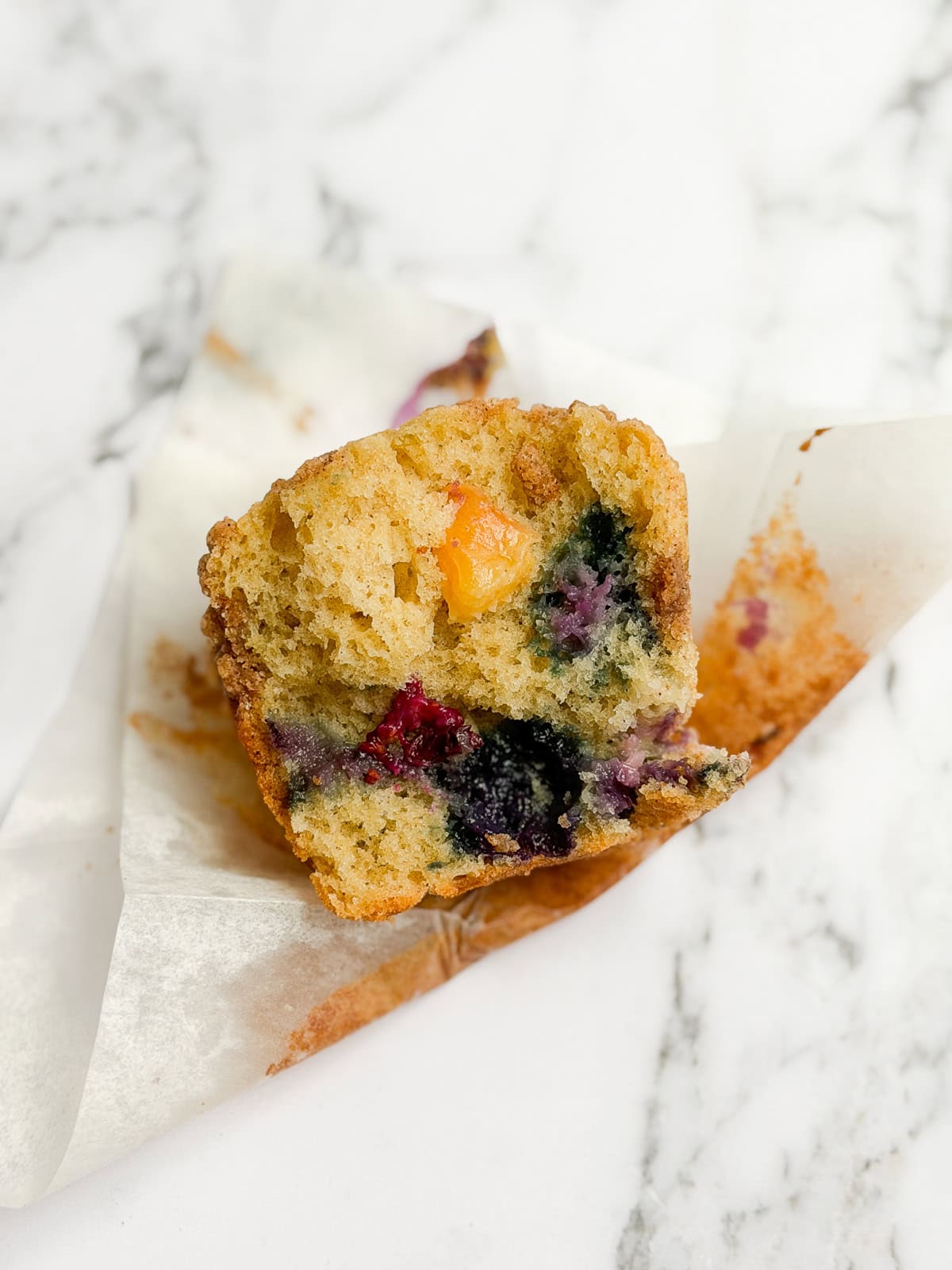 a single blueberry peach muffin broken In half to see inside.
