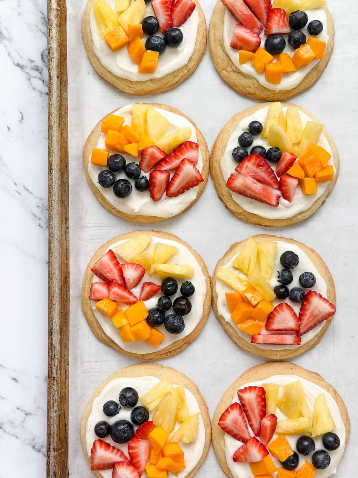 a few of the sugar cookie fruit pizzas on a cookie sheet.