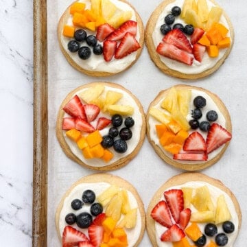 a few of the sugar cookie fruit pizzas on a cookie sheet.