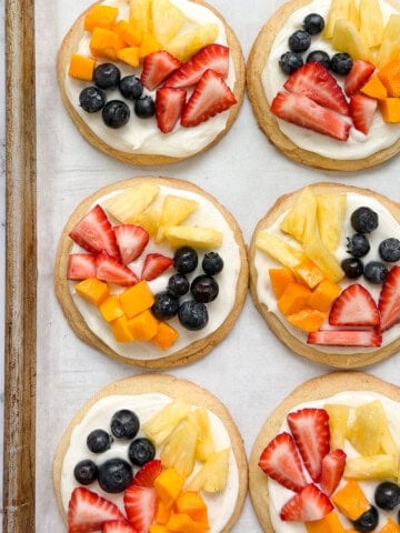 a few of the sugar cookie fruit pizzas on a cookie sheet.