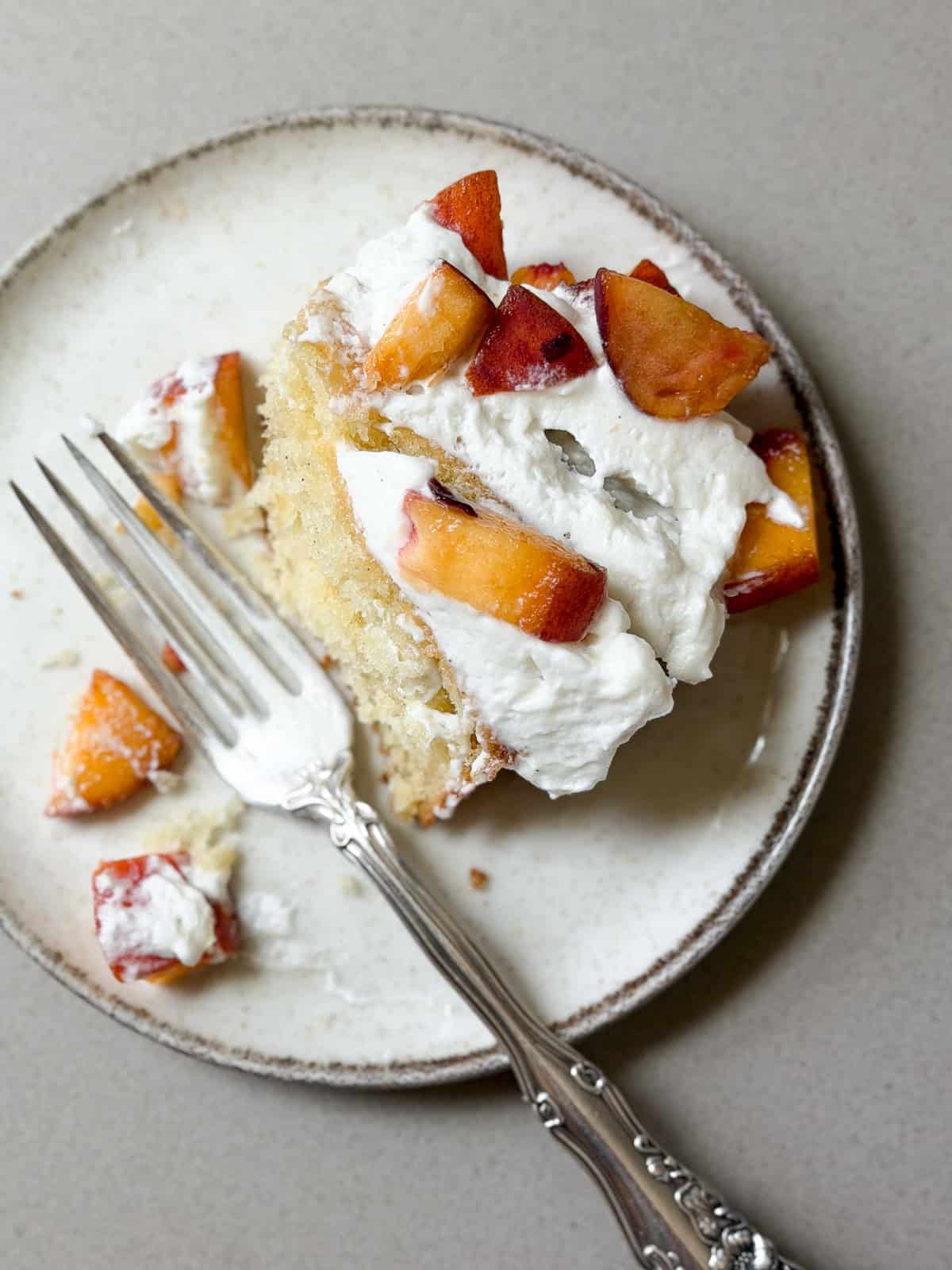 a single piece of peaches and cream cake on a plate with a fork and some bites missing.